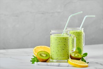 Two glasses with kiwi and lemon smoothie with mint on marble background and slices of fruits