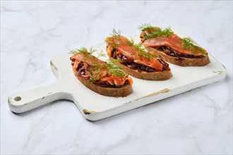 Salmon sandwich with caramelized onion on wooden serving board
