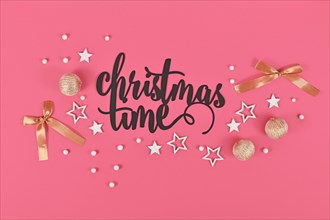 Black 'Christmas time' text next to golden and white bauble and star ornaments on pink background