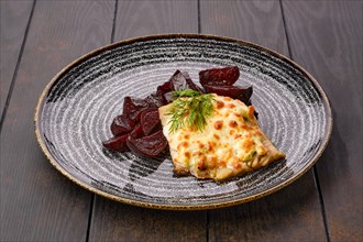 Fried cod fillet with melted cheese topping and roasted beetroot slices on dark wooden table