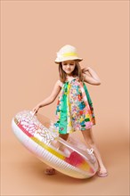 Cute child in sundress and straw hat with swimming ring playing in studio