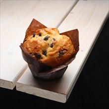 Fresh muffin with raisins in paper wrapper on the corner of wooden table