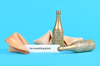 Open fortune cookie with motivational text saying 'Do something great' with golden champagne bottles