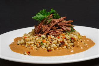 Plate with boiled beef and pearl barley on black background