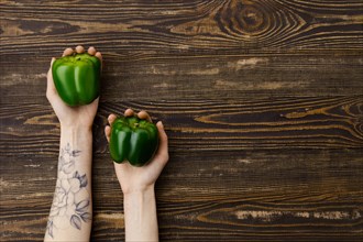 Overhead view of fresh green bell pepper in hands over wooden background