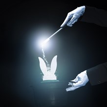 Magician performing trick with magic wand against black glowing background