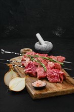 Skewers with raw beef meat and spices on wooden cutting board