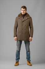 Full length portrait of handsome man in warm winter coat posing in studio