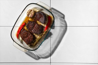 Top view of grilled beef steak in cast iron skillet on ceramic tile background with harsh shadow