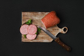 Overhead view of smoked beef salami and sandwich on cutting board over black background