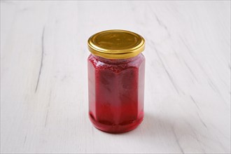 Whole closed jar of cherry jam on white wooden background