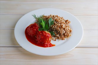 Traditional russian meatballs with buckwheat and tomato sauce on wooden table