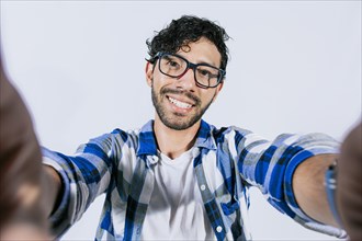 Handsome man taking a selfie looking at the camera on isolated background. Teenage guy taking a self portrait isolated. Guy with beard and glasses taking a self portrait isolated
