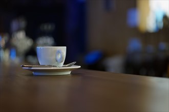 White cup of coffee with steam on wooden table near window