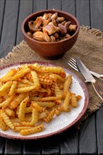 Fried crinkle cut american fries and roasted mushrooms on dark wooden table