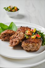Closeup view of fried veal meatballs on a plate with basil and tomato