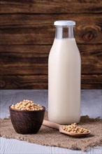 Closed bottle of soy milk with small bowl and spoon with soya beans