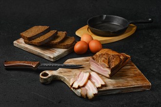 Smoked pork bacon with brown bread and eggs on wooden cutting board
