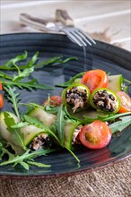 Chopped smoked salmon and black olives rolled in cucumber decorated with tomato and arugula
