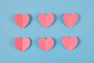 Cute pink paper craft hearts arranged in two rows on pastel blue background