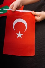 Child hand holding Turkish flag with white star and moon
