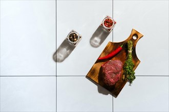 Top view of marinated raw beef steak with spice on ceramic tile with harsh shadow