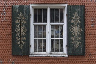 Ornate shutters on a barred window on a shingle facade