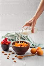 Female hand pouring milk in muesli with apricots and almonds