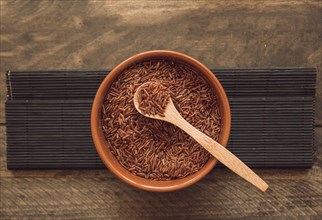 Red jasmine rice grains bowl against wooden backdrop