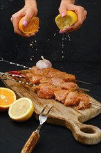Pouring orange and lemon juice on skewers with raw turkey meat with sweet and spicy rub on dark background