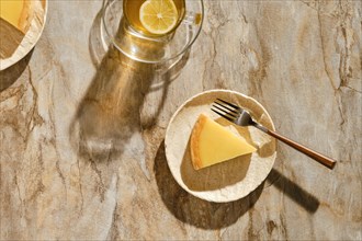 Top view of piece of lemon tart with tea under direct sunlight with hard shadows on the table