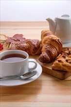 Puff pastry raisin bun and crispy croissant on wooden table with tea