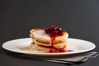 Plate with pancakes with sour cream and cherry syrup on black background