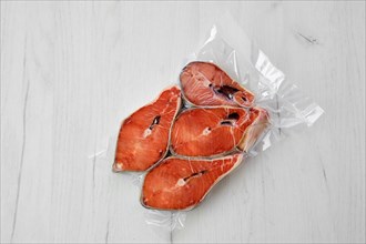 Overhead view of raw salmon steak in vacuum packaging on light background