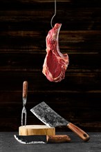Beef ribeye steak bone-in on steel hook over the forged butcher set
