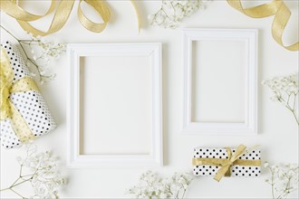 Golden ribbon gift boxes baby s breath flowers near wooden frame white backdrop