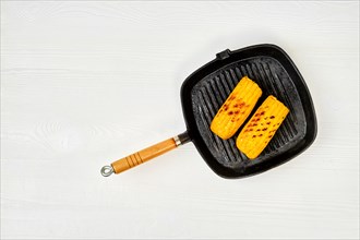 Top view at cast iron pan with grilled corn on white wooden table