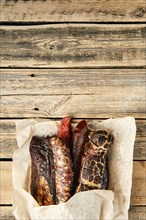 Smoked and dried meat and sausages sticking out of wrapping paper on wooden table
