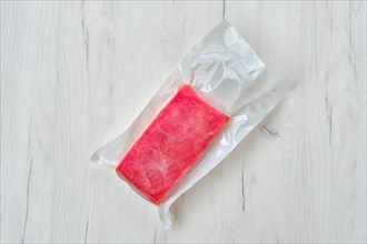 Raw frozen tuna fillet in vacuum packaging on wooden background