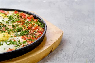 Closeup view of eggs with bell pepper and tomato baked in oven in cast-iron skillet