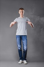 Middle age man in jeans pointing fingers to his t-shirt on gray background
