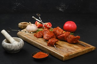 Skewers with marinated raw pork meat on wooden board on dark background