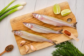 Top view of raw fresh smelt fish on wooden cutting board with spice and herbs