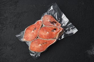 Overhead view of raw salmon steak in vacuum packaging on dark background
