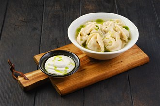 Bowl with pork pelmeni with sour cream on a wooden serving board
