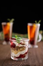 Delicious tiramisu dessert with cherry and citrus tea on dark wooden background