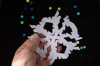 Snowflake shaped paper in hand on bokeh light background