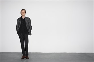 Man in wool jacket standing near white concrete wall with hands in pocket