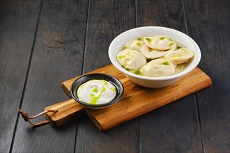 Bowl with beef pelmeni with sour cream on a wooden serving board