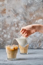 Hand pouring cream in iced coffee in rocks glass